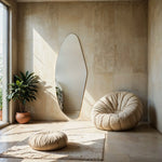 Aurora irregular curve mirror with potted plant and cushioned pouf in modern interior.