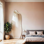 Luna irregular mirror in stylish bedroom with potted plant and bed.