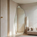 Luna irregular mirror leaning against beige wall near sofa and floor lamp.
