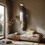 Solis irregular mirror leaning against wall behind beige sofa with pampas grass in sunlit room.