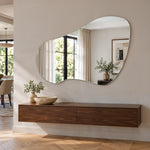 Specchio organico asimmetrico senza cornice Tria sopra una credenza sospesa in noce