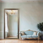 Gold and antique silver baroque full-length wall mirror beside a light blue tufted sofa with a gold chandelier reflected