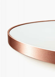 Close-up of eclipse round mirror frame in rose gold finish with brushed metallic texture.