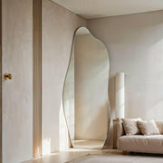 Luna irregular mirror leaning against beige wall near sofa and floor lamp.