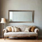 Large gold and antique silver baroque wall mirror above a cream tufted sofa with gold cushions