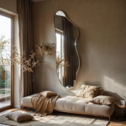 Solis irregular mirror leaning against wall behind beige sofa with pampas grass in sunlit room.