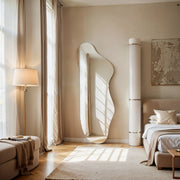 Solis irregular mirror standing in sunlit living room with floor lamp, sofa and bed.