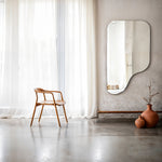 Specchio alto asimmetrico senza cornice Stilla su una parete intonacata con sedia in legno e vasi in terracotta